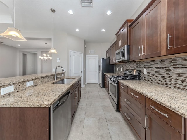 kitchen featuring stainless steel appliances, a sink, visible vents, light stone countertops, and decorative light fixtures