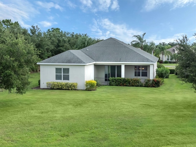 back of property featuring roof with shingles, a lawn, and stucco siding