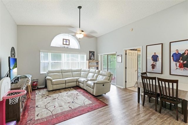 living room featuring ceiling fan, wood-type flooring, high vaulted ceiling, and a textured ceiling