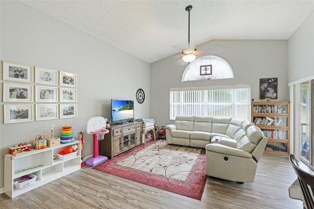 living room with ceiling fan, wood-type flooring, high vaulted ceiling, and a textured ceiling