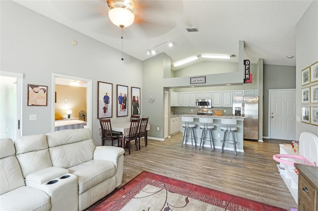 living room featuring rail lighting, high vaulted ceiling, a textured ceiling, ceiling fan, and light hardwood / wood-style floors