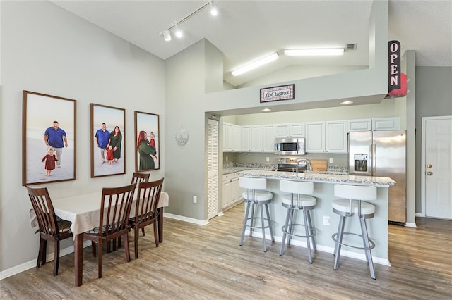 kitchen with stainless steel appliances, a kitchen breakfast bar, a center island, light stone countertops, and white cabinets