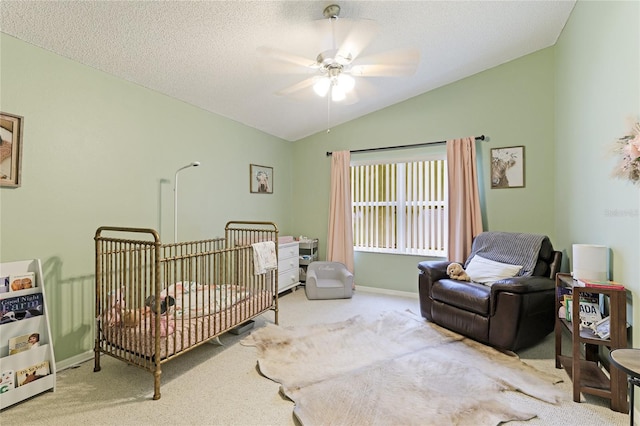 bedroom featuring vaulted ceiling, light colored carpet, ceiling fan, a crib, and a textured ceiling