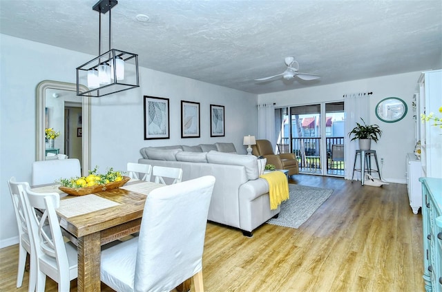 dining space featuring a textured ceiling, ceiling fan with notable chandelier, and light wood-type flooring