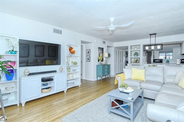 living room featuring light wood finished floors, built in features, visible vents, ceiling fan, and a textured ceiling