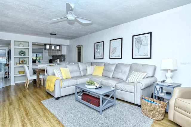 living area featuring a textured ceiling, ceiling fan, built in shelves, and wood finished floors