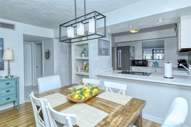 dining space with light wood finished floors, visible vents, and a textured ceiling