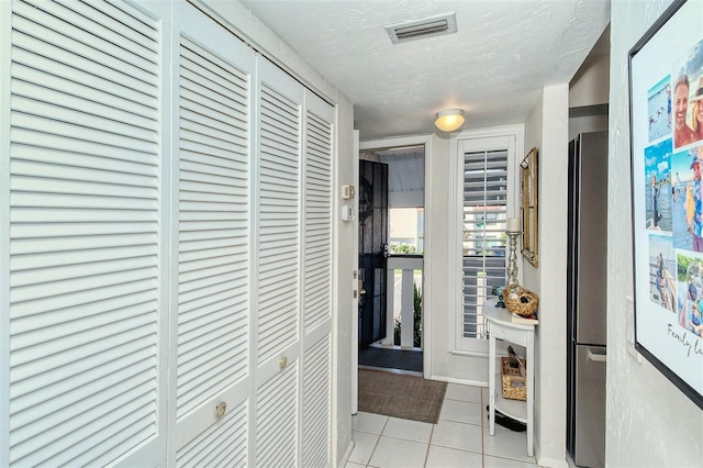 hallway with light tile patterned floors, a textured ceiling, and visible vents