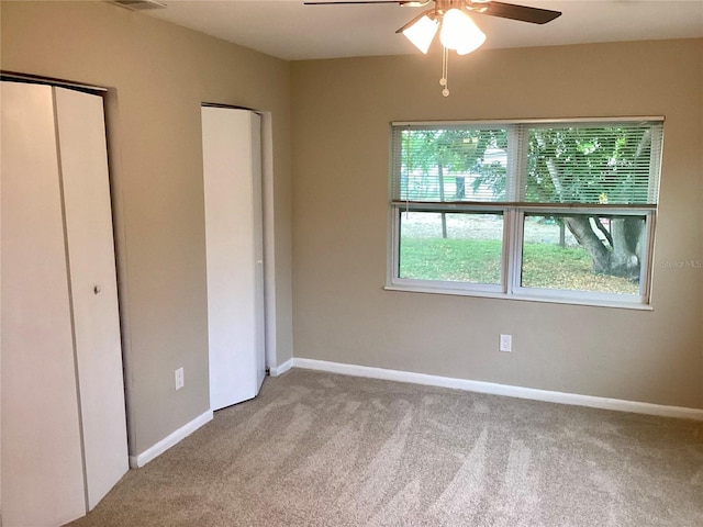 unfurnished bedroom with multiple closets, ceiling fan, and light colored carpet