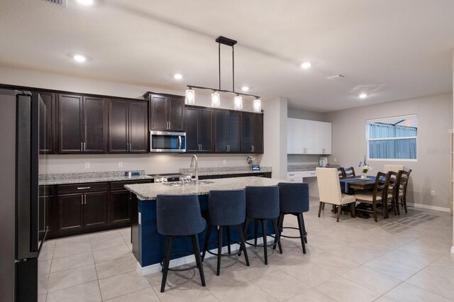 kitchen with appliances with stainless steel finishes, sink, light stone counters, light tile patterned floors, and an island with sink