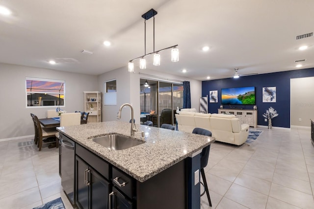 kitchen featuring sink, light stone counters, stainless steel dishwasher, pendant lighting, and a kitchen island with sink