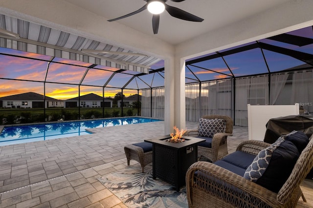 pool at dusk with ceiling fan, a lanai, a patio area, and an outdoor living space with a fire pit