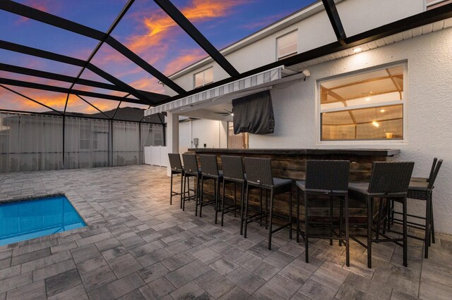 patio terrace at dusk featuring a bar and glass enclosure