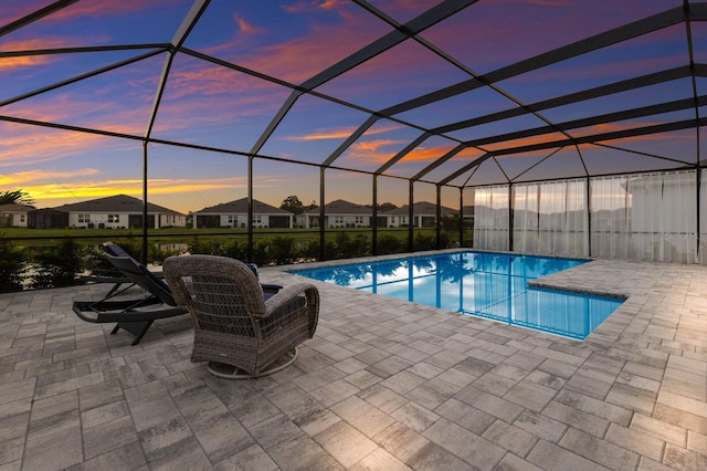 pool at dusk featuring a patio and a lanai