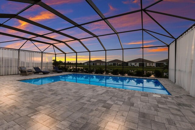 pool at dusk with a patio area and glass enclosure