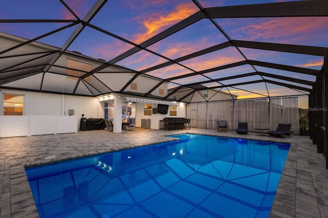 pool at dusk with a lanai and a patio area