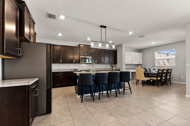 kitchen featuring decorative light fixtures, dark brown cabinets, a breakfast bar, a textured ceiling, and a kitchen island with sink