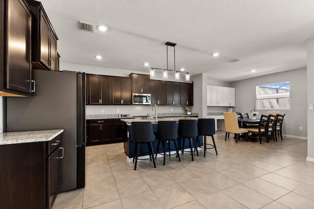 kitchen featuring dark brown cabinetry, a breakfast bar, hanging light fixtures, an island with sink, and stainless steel appliances