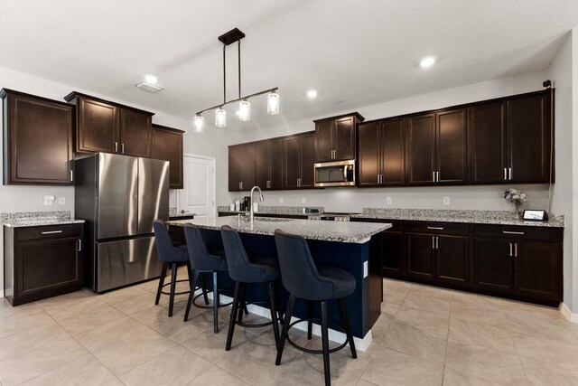 kitchen featuring light tile patterned flooring, light stone counters, dark brown cabinetry, and appliances with stainless steel finishes