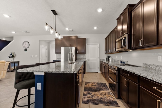 kitchen featuring stainless steel appliances, an island with sink, dark brown cabinetry, and a kitchen bar