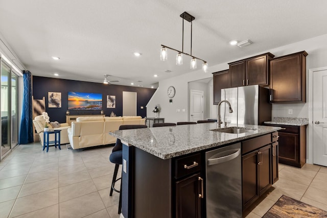 kitchen with ceiling fan, an island with sink, sink, light stone countertops, and track lighting