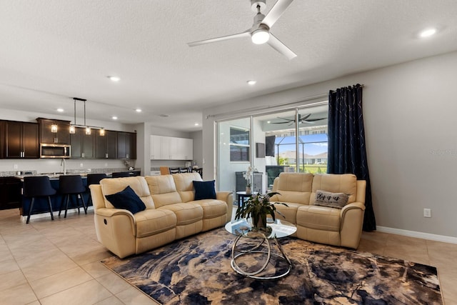 living room featuring a textured ceiling, sink, light tile patterned floors, and ceiling fan