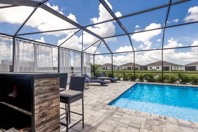 view of pool with a patio, glass enclosure, and exterior bar