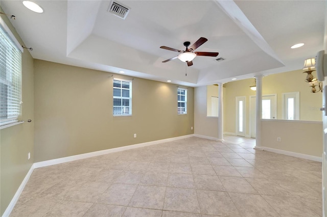 tiled empty room featuring a tray ceiling, ornate columns, and ceiling fan