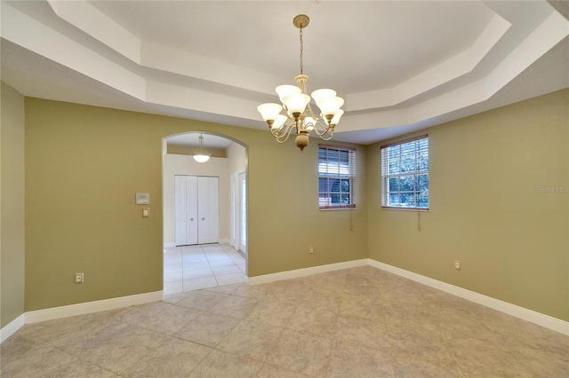 spare room featuring a raised ceiling, light tile patterned floors, and a chandelier