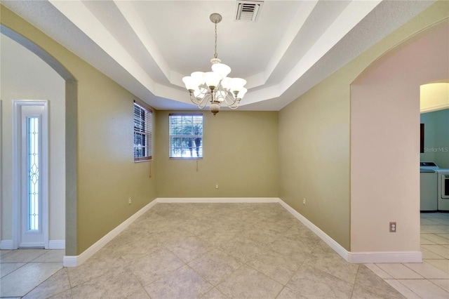 tiled empty room featuring washer and dryer, a tray ceiling, and a chandelier