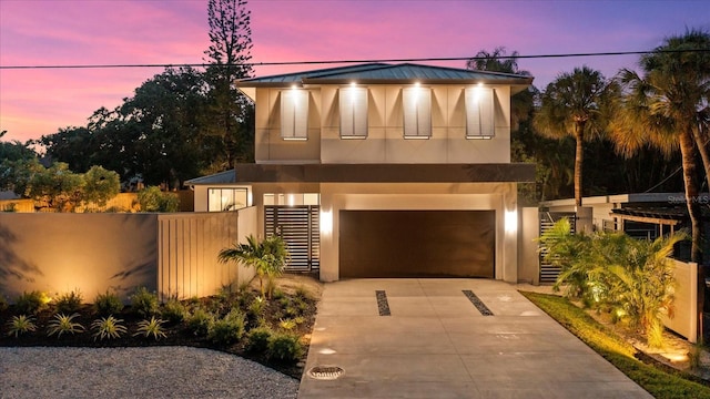 modern home with a garage, concrete driveway, fence, and stucco siding