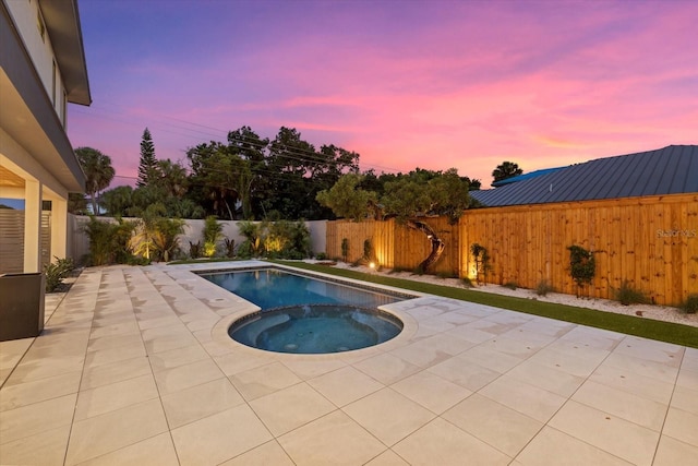 pool at dusk featuring a patio area, a fenced backyard, and a pool with connected hot tub