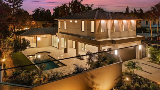 back of house featuring metal roof, a patio, a garage, driveway, and a standing seam roof