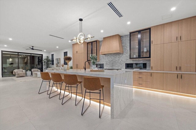 kitchen featuring a center island with sink, light countertops, hanging light fixtures, custom range hood, and visible vents