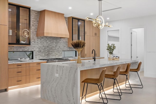 kitchen featuring premium range hood, modern cabinets, backsplash, and decorative light fixtures