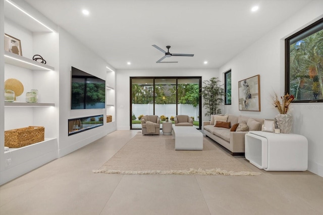 living room with concrete flooring, a glass covered fireplace, built in shelves, and recessed lighting