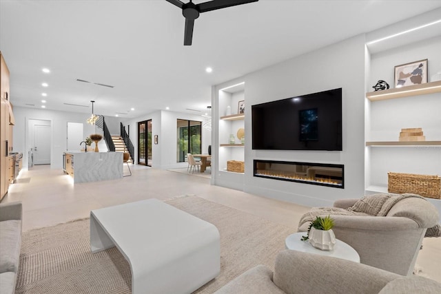 living area with a glass covered fireplace, ceiling fan, stairs, built in shelves, and recessed lighting