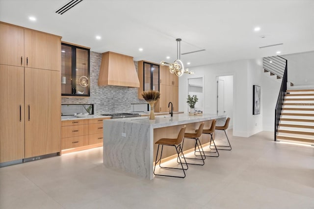 kitchen with glass insert cabinets, custom exhaust hood, a center island with sink, and modern cabinets