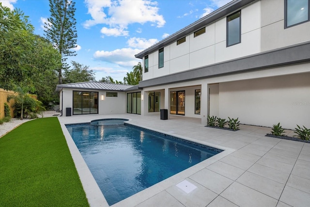 rear view of property featuring a standing seam roof, metal roof, a hot tub, and stucco siding