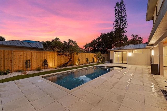 pool at dusk with a patio, a fenced backyard, and a fenced in pool