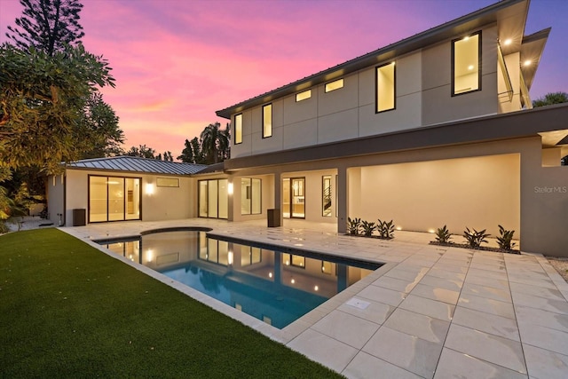 rear view of house with stucco siding, a lawn, a patio area, metal roof, and an outdoor pool