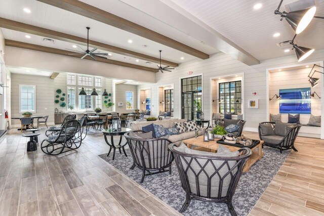 living room with ceiling fan, beamed ceiling, and wood walls