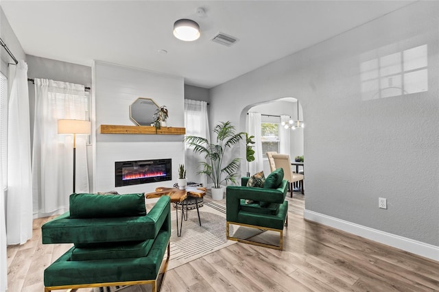 sitting room with arched walkways, a large fireplace, wood finished floors, visible vents, and baseboards