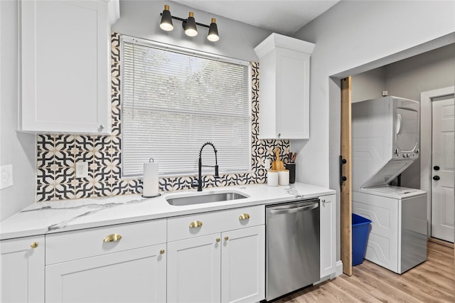 kitchen with a sink, white cabinetry, light wood-style floors, dishwasher, and stacked washer and clothes dryer