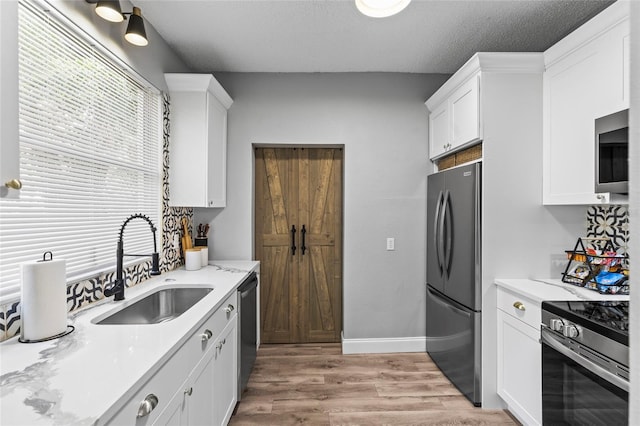 kitchen with a textured ceiling, a sink, white cabinetry, appliances with stainless steel finishes, and light wood finished floors