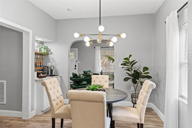 dining space with arched walkways, a notable chandelier, visible vents, light wood-style floors, and baseboards