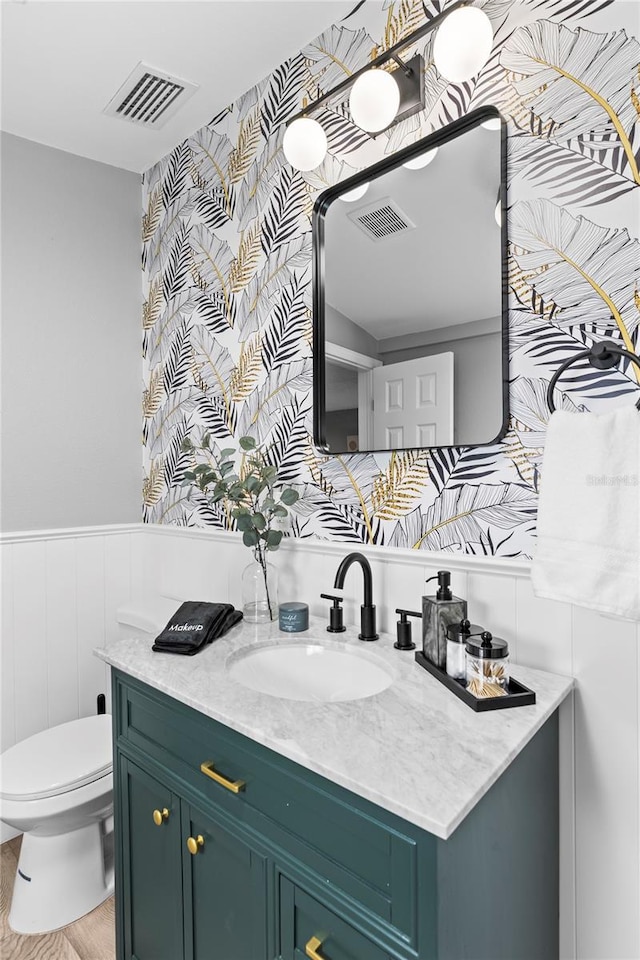 bathroom with toilet, wainscoting, vanity, and visible vents