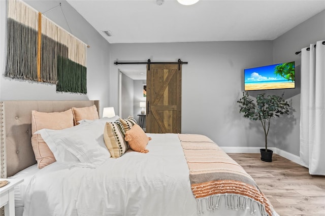 bedroom featuring baseboards, visible vents, light wood finished floors, and a barn door