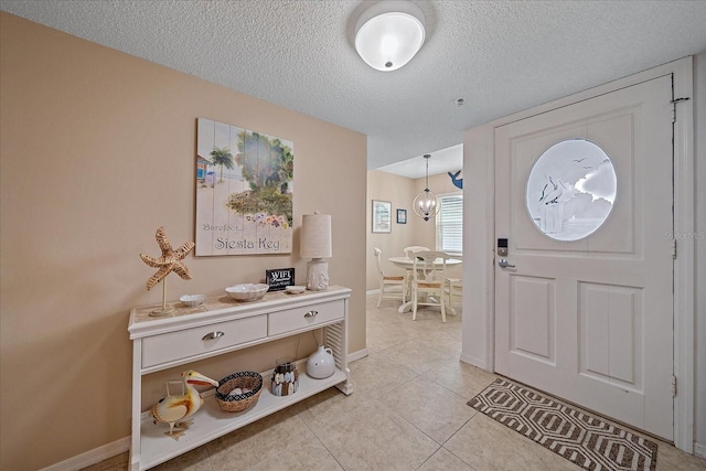 foyer entrance featuring an inviting chandelier, light tile patterned floors, and a textured ceiling