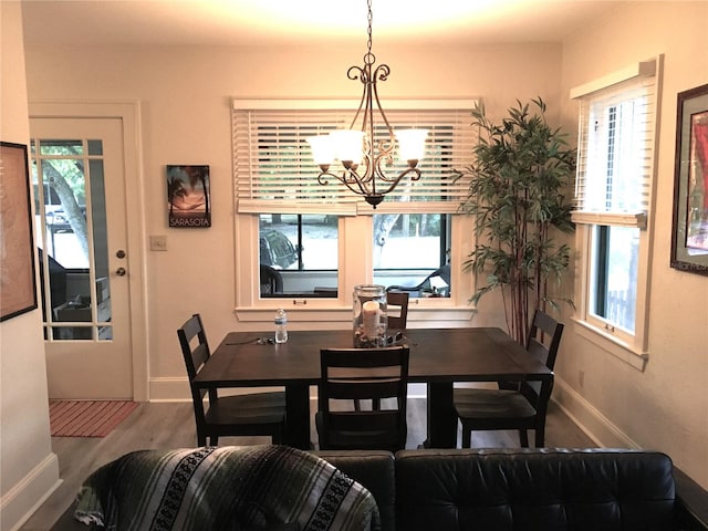 dining room featuring a healthy amount of sunlight, wood-type flooring, and an inviting chandelier